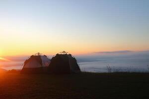 two tents for camping on top of mountain with sea of mist and sunshine in the morning. photo