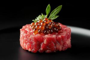 Exquisite steak tartare garnished with fish roe and herbs on black plate photo