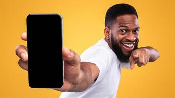 Mobile App Advertisement. Excited Black Man Showing Smartphone Empty Screen Recommending App Posing Over Yellow Studio Background, Smiling To Camera. Check This Out, Cellphone Display Mockup photo