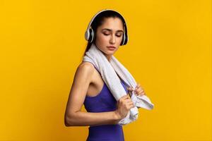 Music For Motivation. Portrait Of Determined Young Sportive Lady Wearing Wireless Headset Listening To Playlist Standing Isolated Over Orange Studio Background With White Towel Aroung Neck photo