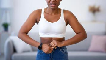 Frustrated Black Woman Buttoning Small Jeans After Weight Gain Standing At Home, Looking At Camera. Slimming Issue, Visceral Fat And Cellulitis, Weight-Loss Problem Concept photo