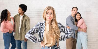 Loneliness in company of friends and sad facial emotions. Frustrated zoomer lady looking away, near happy international couples hugging, on white wall background, studio shot, empty space, panorama photo