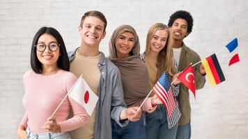 Exchange students and language school for different people. Funny digital young international pupils holding flags of USA, Japan, Turkey, Germany and France in classroom, studio shot, empty space photo