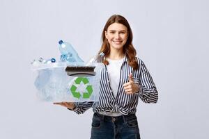 A young woman smiles while holding a recycling box filled with plastic bottles. She promotes eco-friendly practices and showcases her commitment to sustainability in an indoor setting. photo
