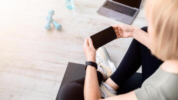 Unrecognizable senior woman using smartphone with empty screen after home workout, mockup for design. Mature lady holding mobile device with space for your app or website after domestic training photo