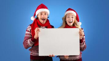 Christmas ad. Excited millennial couple holding empty poster with mockup for design over blue background photo