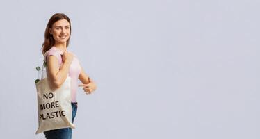 A woman stands confidently, holding a tote bag that says No More Plastic. She promotes recycling and eco-friendly practices, reflecting her commitment to sustainability, copy space photo