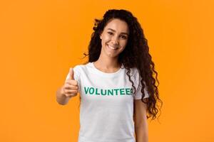 Volunteer Woman Showing Like Gesturing Thumbs Up Standing On Yellow Studio Background, Smiling To Camera. I Approve Charity Work And Volunteering Concept photo