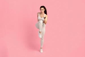 Running Competition. Full length front vertical portrait of confident young woman in sportswear running and looking towards camera, isolated over pink studio background. Lady jogging and sprinting photo