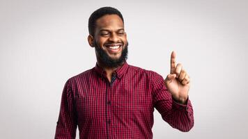 Look At This. Smiling African American Man Holding Invisible Object On Finger Advertising Your Product Or Pointing Finger Up Posing Standing Over White Studio Background photo