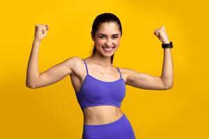 Winner. Portrait of excited young woman in sportswear celebrating triumph, raising clenched fists in the air isolated over orange yellow studio background. Happy smiling lady posing photo