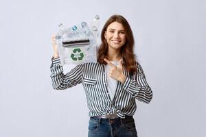 Cheerful Volunteer Woman Pointing At Container With Plastic Waste For Recycling In Her Hands, Smiling Millennial Lady Promoting Garbage Sorting And Eco-Friendly Living, Standing On Gray Background photo