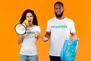 Don't Litter. Two Emotional Volunteers Shouting In Megaphone Holding Blue Garbage Bag Standing Over Yellow Background In Studio, Looking At Camera. Stop Using Plastic Concept photo