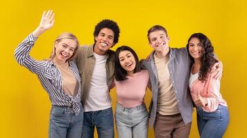 Education at university or college abroad. Cheerful young multiracial international students have fun, laughing, hugging and waving to camera isolated on orange background, copy space, studio shot photo
