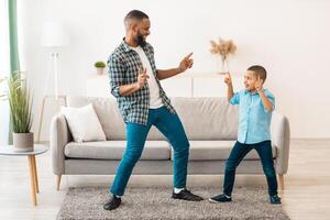 Cheerful African American Dad And Little Son Dancing Having Fun Together Partying At Home On Weekend. Fatherhood Joy, Family Leisure Concept. Full Length Shot Of Daddy And Kid Boy Dance Indoor photo