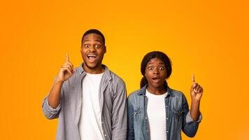 Idea Concept. Exciyed African American Couple Pointing Fingers Up While Standing Isolated Over Yellow Background, Inspired Emotional Black Man And Woman Found Problem Solution, Copy Space photo