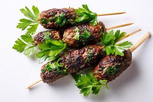 Delicious grilled kofta skewers topped with parsley served on clean white surface photo