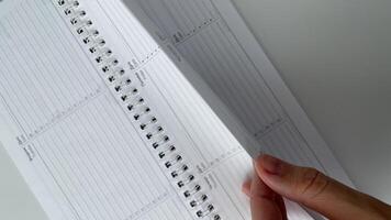 Close-up of a hand turning the pages of a blank spiral planner, perfect for illustrating organization, planning, and productivity concepts. This clean and modern image is ideal for business, education, and time management projects. Use this photo to inspi