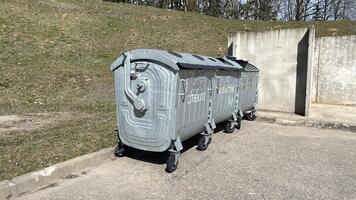 Three gray garbage bins for separate waste disposal stand on a vacant lot. Green grass and sunny weather photo