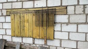 grill for roasting meat hangs on a nail in the yard of the house, against the background of a white brick wall, an old wooden stepladder stands below, yellow planks photo