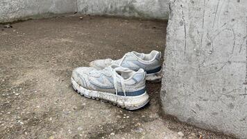 A pair of dirty white sneakers leaning against a wall photo