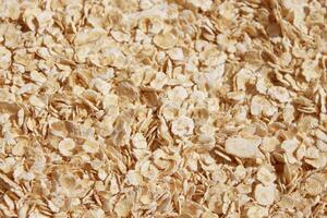 Rolled oats background. Evenly sprinkled raw thick-rolled oats close-up, background photo