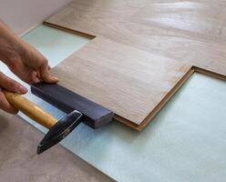 Repair, Improvement of the House and Office with Their Own Hands. Close-up of a Hand With a Rubber Mallet Laying a Light Wood laminate in the Living Room. Worker. Laying Process photo