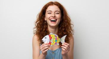 A young woman laughing while holding an April fish in her hands, enjoying a playful moment. photo