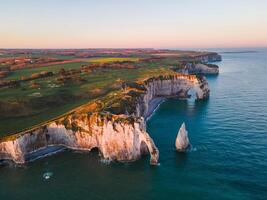 Iconic chalk cliffs and turquoise waters of Etretat glow under sunlight, showcasing Normandy's natural beauty and peaceful coastline. photo