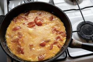 scrambled eggs with tomatoes in a frying pan on a gas stove photo