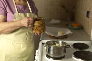 The hands of a senior woman add salt to sweet butter on the stove photo
