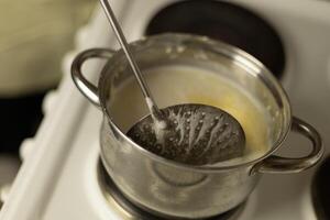 stirring sweet cream ghee in a saucepan with a metal spoon with holes photo