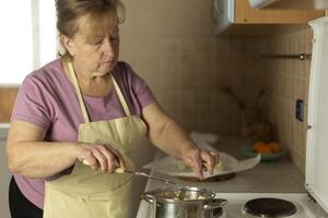 Senior woman in apron adding sweet butter to a pan to melt, making ghee photo