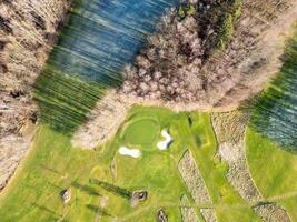 Elevated perspective of a well-maintained golf course surrounded by trees. The lush green fairways and sand traps are visible under clear skies. Ideal for golfing enthusiasts. photo
