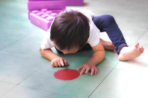 A little boy is interested in the red circle symbols on the floor that mark each group of toys. 2-year-old Asian child. photo