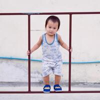 Asian toddler boy having fun climbing on iron fence, toddler happiness, muscle development, happy kid smiling and looking at camera. 2 year old son. photo