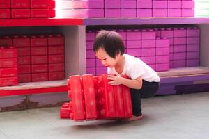 Asian boy playing with big red building blocks, child moving toys, learning through play, development of muscles of different parts of the body. 2 year old son. photo