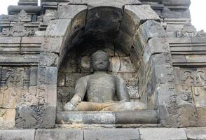 A Buddha statue sits calmly in a stone niche on Borobudur temple, surrounded by ancient carvings. photo