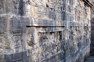 Ancient stone wall carvings with intricate figures line a temple corridor. photo