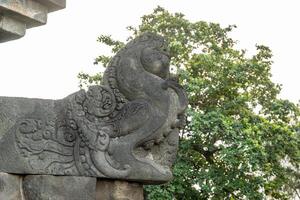 A detailed stone carving of a mythical creature at Borobudur, with trees in the background. photo