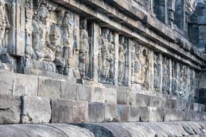 Ancient stone carvings on a temple wall, depicting standing and seated human figures. photo