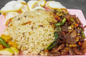 Fried rice with stir-fried vegetables, crackers, and pickles on a pink plate. photo