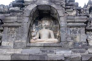 A headless stone Buddha statue sits in a carved niche of Borobudur Temple. photo