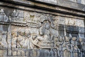 A stone relief shows a seated figure surrounded by followers in detailed ancient temple carvings. photo
