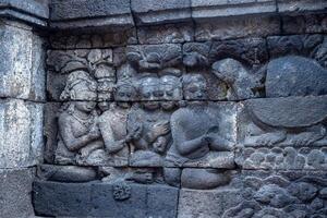 Ancient stone relief showing seated figures and animals in a storytelling scene. photo