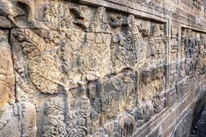Stone wall carvings show ancient scenes with trees, people, birds, and animals in fine detail. photo