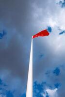 Red Flag on Tall Pole Against Blue Sky with Clouds A Stunning Vertical Photograph photo