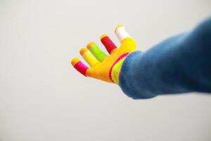 A vibrant hand, covered in a colorful glove with rainbow accents and painted fingertips against a stark white backdrop photo