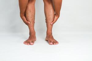 Man holds his legs, expressing leg pain or muscle cramp issues on a plain background photo