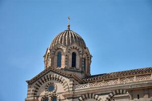 Dome and architectural details of Notre Dame de la Garde in Marseille, France, under a clear blue sky and intense natural light photo